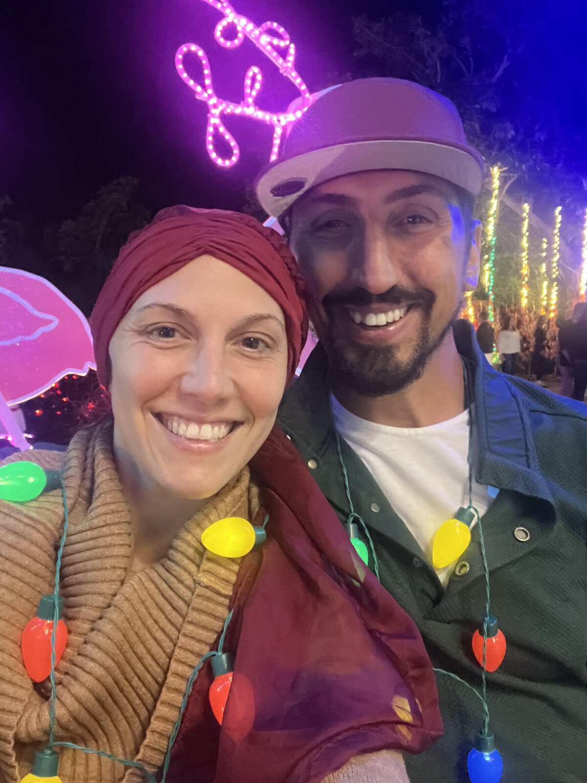 Adelina and her husband at a night-time light display, both wearing necklaces of glowing light bulbs